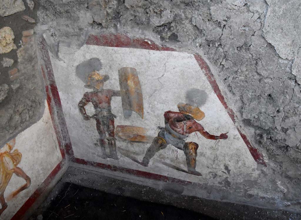 Two gladiators at the end of the fight, one wins the other succumbs.
The fresco of about 1.12 meters x 1.5 meters, found in a room behind the widening of the intersection of the Vicolo dei Balconi and the Vicolo delle Nozze D’Argento, has a trapezoidal shape, as it was located in the basement, perhaps of a shop. Above the painting we can see the imprint of the wooden staircase. 
It is very likely that this place was frequented by gladiators, it is in the Regio V, not far from the caserma dei gladiatori from where, among other things, come the highest number of graffiti inscriptions related to their world. In this gladiatorial fresco of a Murmillo and a Thracian, of particular interest is the extremely realistic representation of the wounds, such as that on the wrist and chest of the succumbing gladiator, which let out the blood that also bathes the legs.  We don't know what the final outcome of this fight was. You could die or have grace. In this case there is a singular gesture that the wounded Thracian makes with the hand, perhaps, to plead for salvation; it is the gesture of ad locutia, usually made by the emperor or the general to grant grace.
Due gladiatori al termine del combattimento, l’uno vince l’altro soccombe
L’affresco di circa 1,12 mt x 1,5mt, rinvenuto in un ambiente alle spalle dello slargo di incrocio tra il Vicolo dei Balconi e il vicolo delle Nozze d’Argento, ha forma trapezoidale, in quanto era collocato nel sottoscala, forse di una bottega. Si intravede al di sopra della pittura, l’impronta della scala lignea.
E’ molto probabile che questo luogo fosse frequentato da gladiatori. Siamo nella Regio V, non lontani dalla caserma dei gladiatori da dove, tra l’altro, provengono il numero più alto di iscrizioni graffite riferite a questo mondo. In questo affresco di un Mirmillone e un Trace, di particolare interesse è la rappresentazione estremamente realistica delle ferite, come quella al polso e al petto del gladiatore soccombente, che lascia fuoriuscire il sangue e bagna i gambali.  Non sappiamo quale fosse l’esito finale di questo combattimento. Si poteva morire o avere la grazia. In questo caso c’è un gesto singolare che il trace ferito fa con la mano, forse, per implorare salvezza; è il gesto di ad locutia, abitualmente fatto dall’imperatore o dal generale per concedere la grazia.
http://pompeiisites.org/comunicati/laffresco-dei-gladiatori-combattenti-nuova-scoperta-nella-regio-v/