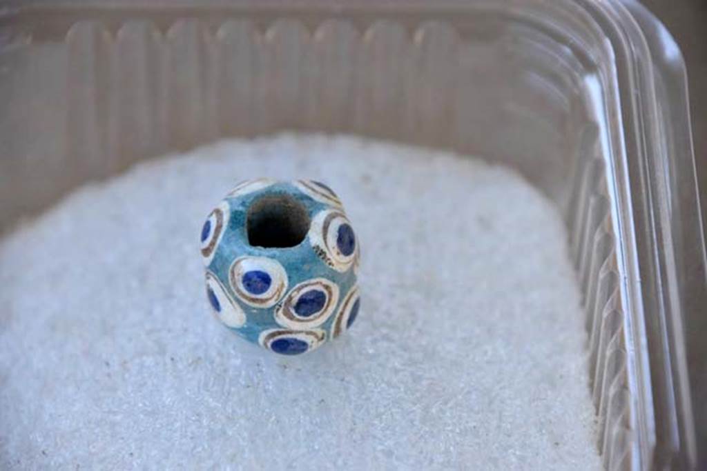 Santuario extraurbano del Fondo Iozzino. 2014 excavations.  A turquoise bead decorated with gold, white and blue ringed patterns.
Una perla turchese decorata con motivi ad anello oro, bianco e blu.
Photograph © Parco Archeologico di Pompei.