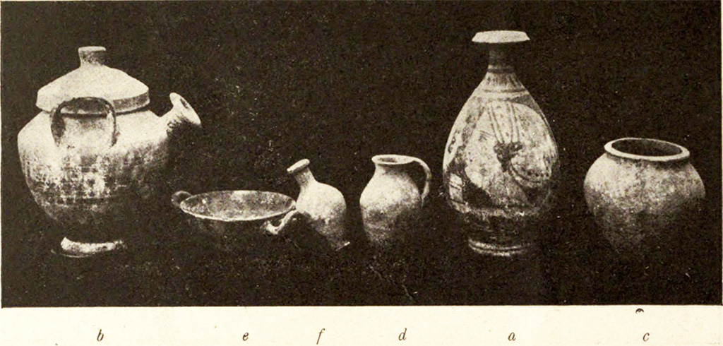 Pompeii Fondo Azzolini. Tomb VI. The photo above shows numerous objects found in the tomb.
b) Pot-bellied pitcher with vertical handles with lid (2):  height 0.20 m., and on the shoulder are the dark slats that are repeated on the lid; between the handles, from the shoulder, protrudes a cylindrical bell-shaped spout. 
e) Black-painted kylix, 0.11m in diameter, in whose bottom are the remains of a floral meander before graffiti and then painted with small white leaves.
f) Rustic ovoid jar with short neck, height 0.09 m. 
d) Rustic flask, height 0.085m., with a shapeless surplus of iron in the base. 
a) Lekythos, oval vessel, high 0.20 m, short neck: On a yellow clay background a female head in profile to the left is painted in black, while the opposite side is a palm between two whorls.
g) Iron blade, length 0.13m., broken in two pieces. 
h) Arc shaped bronze buckle, from a strap. Width 0.027m.
c) Small rustic jar in the form of a dolium, height 0.11m.  
See Notizie degli Scavi di Antichità, 1916, p. 292-3, fig. 3.