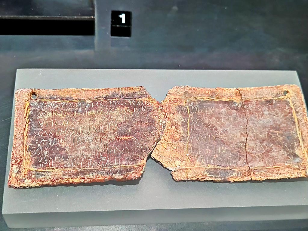 Pompeii Fondo Azzolini. Tomb 10. March 2024. Lead curse tablets. 
According to the exhibition information card this is a tablet with curses from a woman to a freedwoman? Female slave?
Photo courtesy of Giuseppe Ciaramella.
On display in exhibition in Palaestra entitled - “L’altra Pompei, vite comuni all’ombra del Vesuvio”