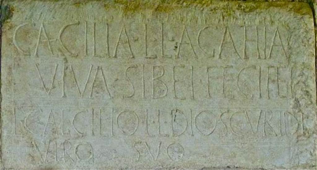 FPND Pompeii. May 2011. Plaque on front of tomb. Photo courtesy of Michael Binns.
The inscription reads
CAECILIA L. L. AGATHIA
VIVA SIBEI FECIT ET 
L. CAECILIO L. L. DIOSCVRIDI
VIRO SVO.
D’Ambrosio and De Caro expand this to:
Caecilia L(uci) l(iberta) Agathia
viva sibei fecit et 
L(ucio) Caecilio L(uci) l(iberto) Dioscuridi
viro suo.
They name the tomb after Caecilia Agathia, the freedwoman of a Lucius Caecilius, and her husband Lucius Caecilius Dioscurides, a freedman of the same patron.
See D’Ambrosio A. and De Caro S., 1988. Römische Gräberstraßen. München: C.H.Beck. p. 206.