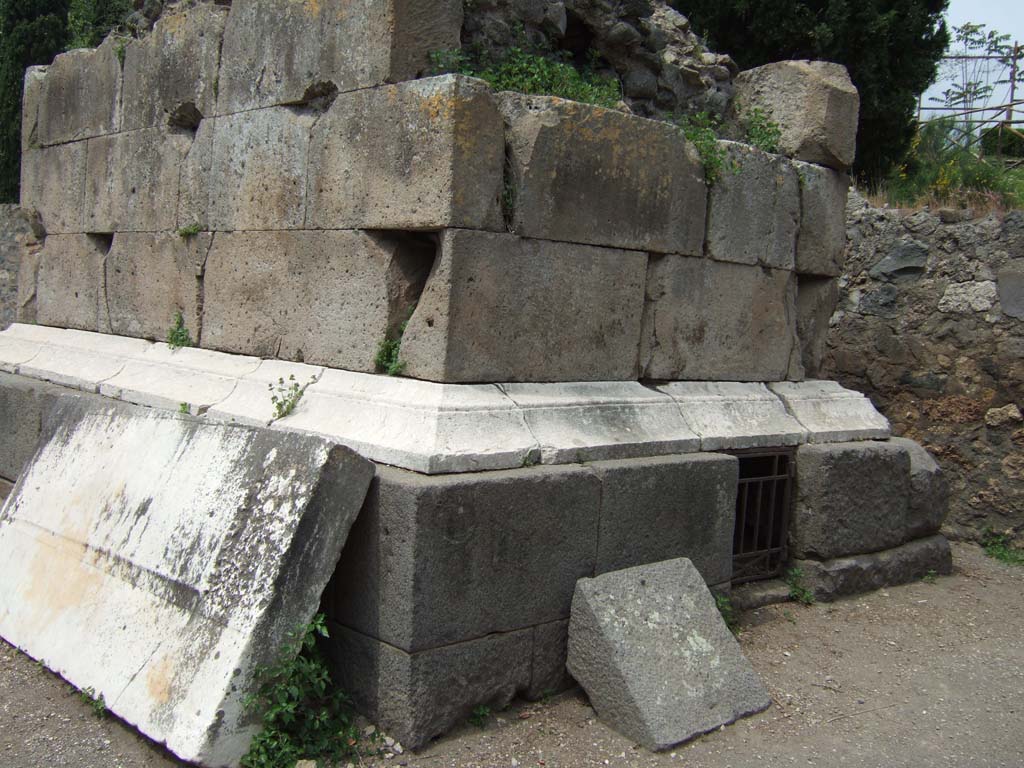 HGE01 Pompeii. May 2006. West side, and south side with doorway to grave chamber. 
In 1887 Sogliano opened the grave chamber and found, covered in earth, two cremation urns enclosed in lead containers. 
Between the bones in the urns was an As of Cn. Piso (c. 23BC), and an As of P. Lurius Agrippa (c. 7BC). 
Also found were the remains of wood work and nails, parts of one of more small boxes richly decorated in ivory, and a broken small clay ointment bottle. 
See Kockel V., 1983. Die Grabbauten vor dem Herkulaner Tor in Pompeji. Mainz: von Zabern. (p.111-5, Taf. 32-33).
According to Garcia y Garcia, a bomb fell near here in September 1943.
This caused the partial destruction and shattering of some blocks of the footings on the east side of this tomb, which had not yet been finished in 79AD.
See Garcia y Garcia, L., 2006. Danni di guerra a Pompei. Rome: L’Erma di Bretschneider. (p.160)