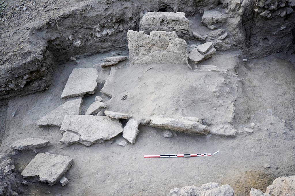 The collapsed slabs of burial SP30055 (HGE31A) being excavated. Taken from the east. 
Photo © B. Lemaire, EFR/CNRS. 
Burial SP30055, shows elements of the fractured and fallen wall slabs (Fig. 24). 
It was a box burial consisting of four monolithic slabs of Sarno limestone placed in the field, delimiting a space in which the deceased and the offerings were placed. 
The levels in place that have come down to us allow us to put forward the hypothesis that the burial is installed in the substratum, most probably with the digging of a pit whose limits are represented by the blocks forming the burial. 
The slabs on the short sides are enclosed by those on the long sides, forming a box and defining a rectangular structure of 2.25 m by 1.40 m (maximum), oriented north-east/south-west.
The north-western wall, which is better preserved (31.94 m s.l.m.), makes it possible to restore the height and thus the internal space of the tomb: 1.94 m by 0.98 m, for a height of 1.08 m.
(See CEFR 1581 and below) Para 42, Fig. 24.
Les dalles effondrées de la sépulture SP30055 en cours de fouille. Pris de l’est. 
Photo © B. Lemaire, EFR/CNRS. 
La sépulture SP30055, présente des éléments des dalles des parois fracturées et tombées au sol (fig. 24). 
Il s’agissait d’une sépulture à caisse matérialisée par quatre dalles monolithes en calcaire du Sarno posées de champ, délimitant un espace dans lequel sont installés le défunt et les offrandes. 
Les niveaux en place qui nous sont parvenus permettent d’avancer l’hypothèse que la sépulture est installée dans le substrat, très probablement avec le creusement d’une fosse dont les limites sont représentées par les blocs formant la sépulture. 
Les dalles des petits côtés sont enserrées par celles des grands côtés, formant un coffre et définissant une structure rectangulaire de 2,25 m sur 1,40 m (au maximum), orientée nord-est/sud-ouest.
La paroi nord-ouest, mieux conservée (31,94 m s.l.m.), permet de restituer la hauteur et ainsi l’espace interne de la tombe : 1,94 m sur 0,98 m, pour 1,08 m de hauteur.
(Voir CEFR 1581 et ci-dessous) Para. 42, Fig. 24.