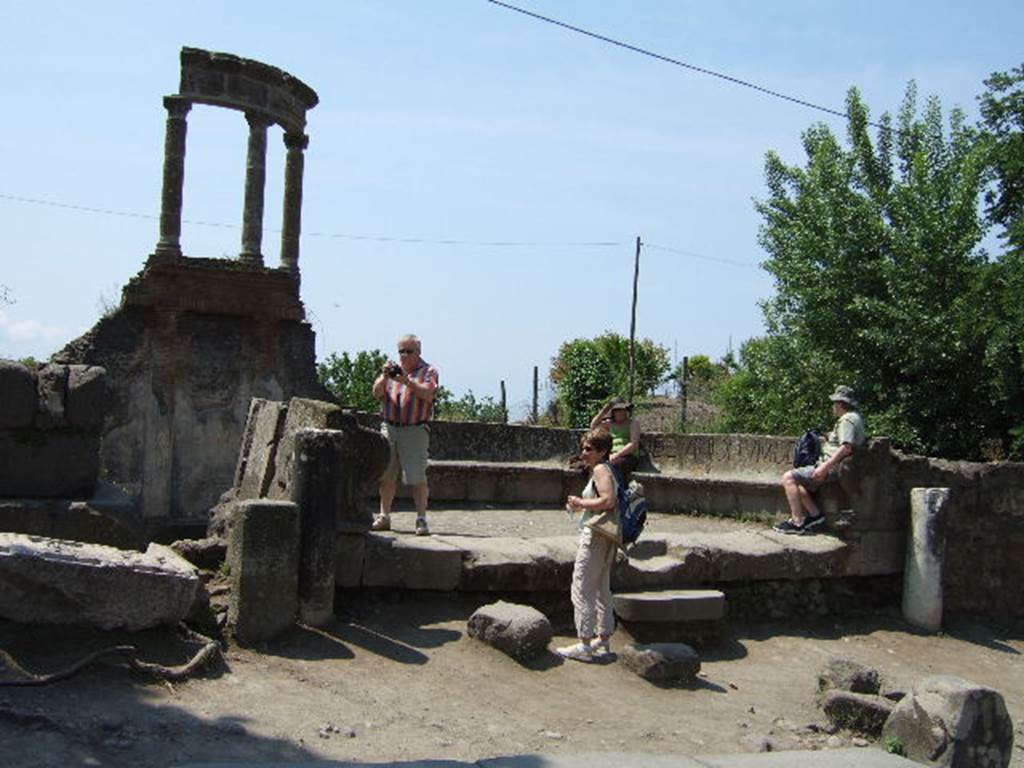 HGW04 Pompeii. May 2006. Looking west towards the schola tomb of Mamia.  
According to PAH, 6 January 1785, the seat with the inscription to the priestess Mammia, which was taken 2nd August 1763 and sent to the Royal Museum at Portici was put back in its original site. 
1785 6 Gennaio - Si rimette nel suo antico sito il sedile di piperno coll’iscrizione della Sacerdotessa Mammia, che ne fu tolto a' 2 agosto 1763, e mandato al R. Museo di Portici.
See Fiorelli, Pompeianarum antiquitatum historia, Vol. 1 1748 to 1818, (p. 167)