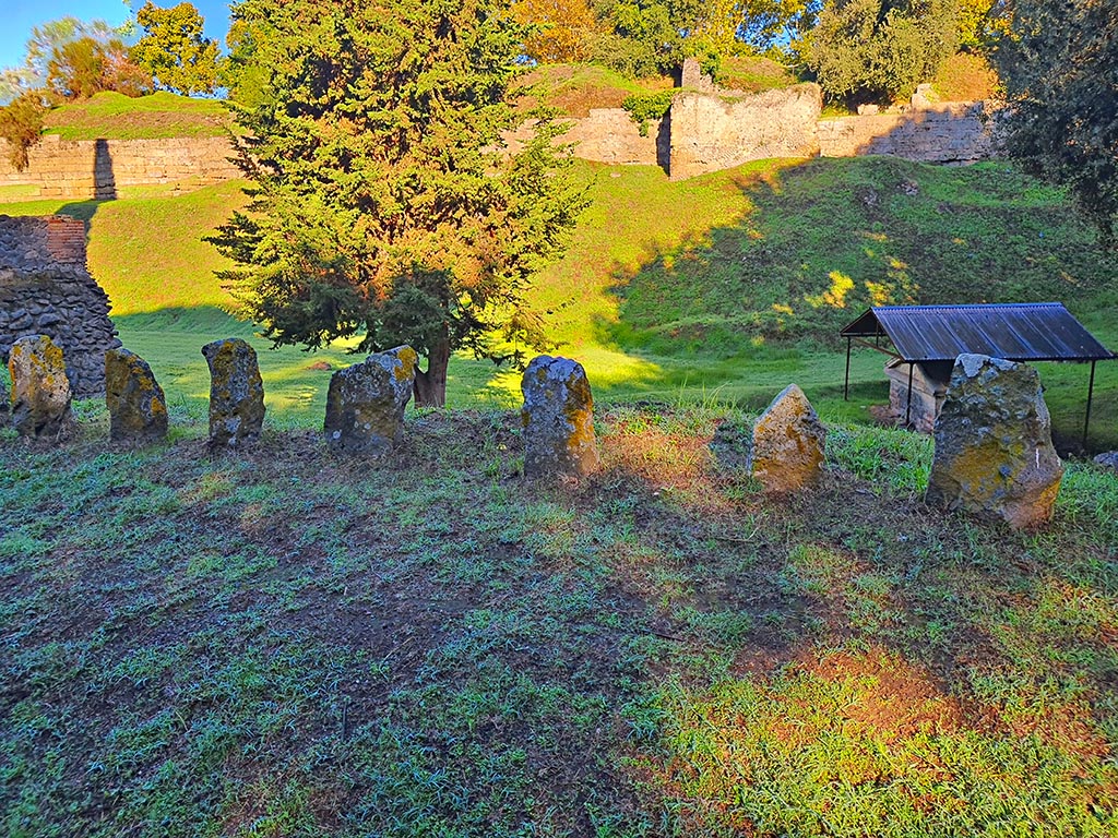 Pompeii Porta Nocera tombs. October 2024. Tomb 34EN, tomb of Afrea Prima?  Looking north on Via delle Tombe.
The tomb has eight cippi, but only seven in the above photo. The seventh one (second from the right) has a triangular top and an inscription
Photo courtesy of Giuseppe Ciaramella.