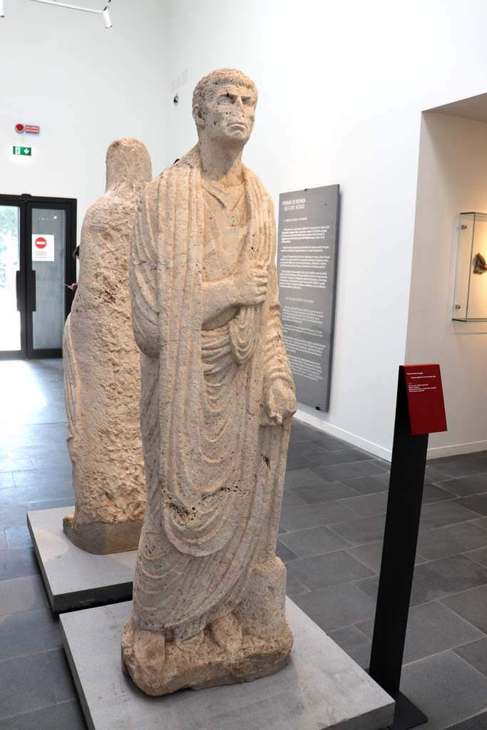 Porta Nocera tombs 34aEN. February 2021. 
Limestone funerary statue of a man wearing a toga, on display in Antiquarium.
Photo courtesy of Fabien Bièvre-Perrin (CC BY-NC-SA).