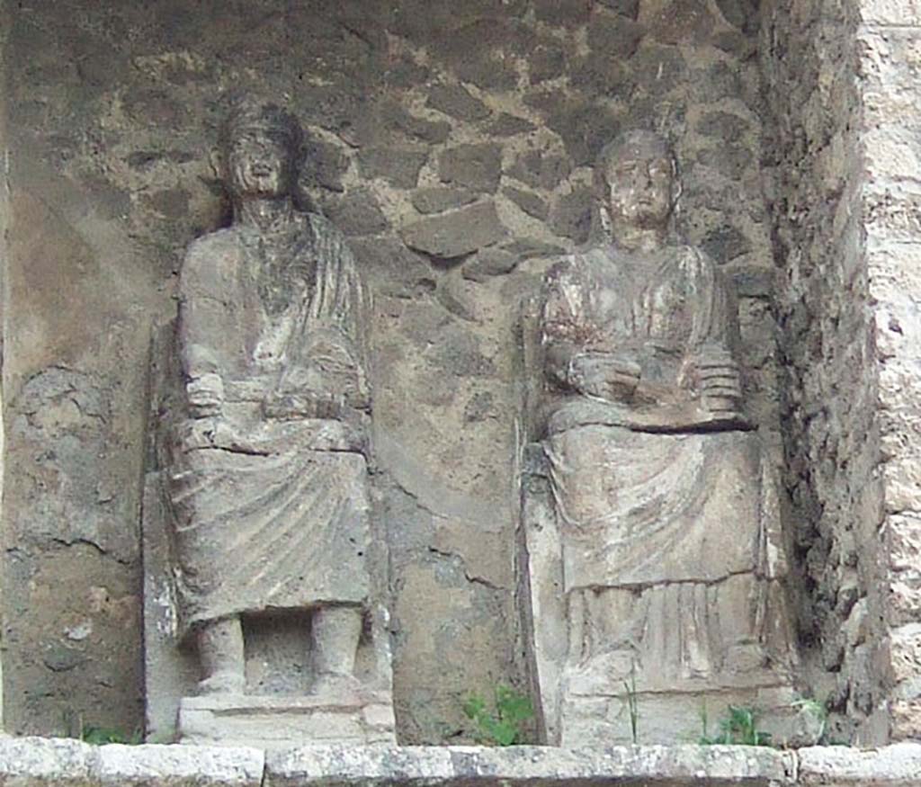 Pompeii Porta Nocera. May 2006. Tomb 9OS. Statues of the seated couple in the tomb.
The couple are destined to remain anonymous as there are no inscriptions.
The roll in the hand of the male character would suggest a function of magistrate who would be well in keeping with the dignity of the monument.
See D’Ambrosio, A. and De Caro, S., 1983. Un Impegno per Pompei: Fotopiano e documentazione della Necropoli di Porta Nocera. Milano: Touring Club Italiano. (9OS)