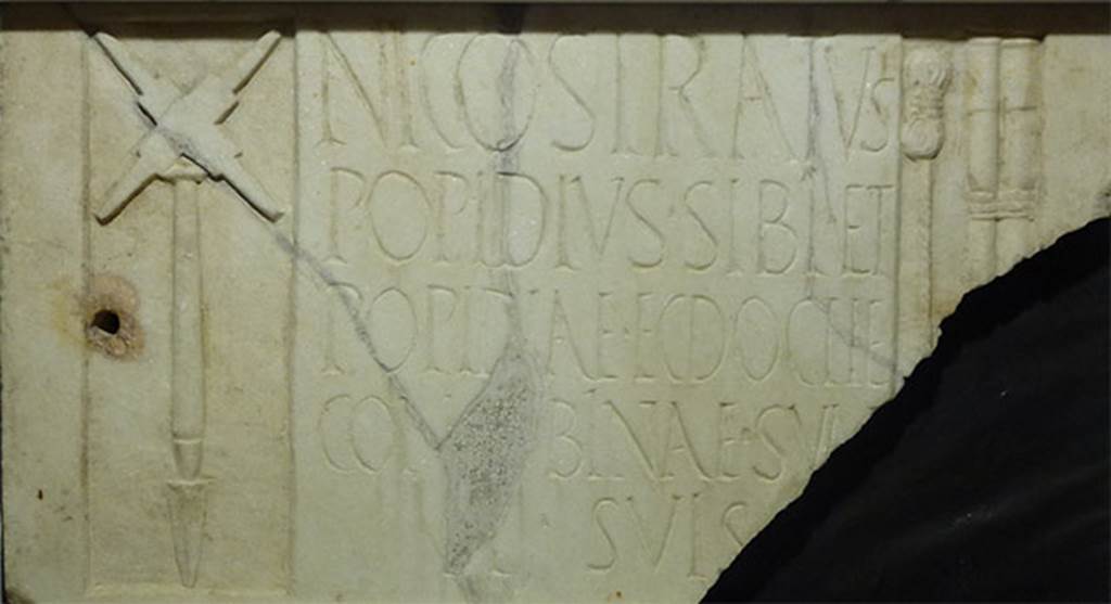 Pompeii Porta Nocera Tomb 17aOS. Found on 13th December 1956. 
Marble relief from the tomb of Popidius Nicostratus with inscription
NICOSTRATVS
POPIDIVS SIBI ET
POPIDIAE ECDOCHE
CONCVBINAE SVAE 
ET SVIS
Photo courtesy of Michael Binns. SAP inventory 11737.
The inscription reads
Nicostratus
Popidius sibi et
Popidiae Ecdoche
Concubinae suae 
et suis
According to Cooley this translates as 
Nicostratus Popidius (erected this monument) for himself and his concubine Popidiae Ecdoche and his family.
See Cooley, A. and M.G.L., 2004. Pompeii : A Sourcebook. London : Routledge. H60b, p. 178.
According to D’Ambrosio, the relief was found in pieces, reused in the floor and vault of the tomb.
It was not therefore related to the tomb.
It represents the tools of a surveyor.
On the left is a representation of a groma. 
On the right is a length of coiled cord and two measuring rods tied together. 
In the incomplete corner was probably a lead plumb line (perpendiculum), which was used with the groma.
See D’Ambrosio, A. and De Caro, S., 1983. Un Impegno per Pompei: Fotopiano e documentazione della Necropoli di Porta Nocera. Milano: Touring Club Italiano. 17a b OS.
According to Sampaolo, the epigrafic characters and the tablets reuse indicate Popidius Nicostratus was probably active in the first decades of the first century d.C./A.D.
Perhaps the grave of Nicostrato, damaged by the 62 earthquake, was not restored anymore.
See Sampaolo V., in Pompei 1748-1980, I tempi della documentazione. p. 206-7.