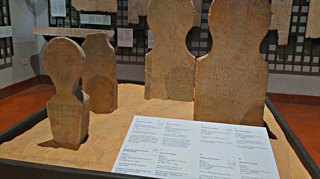 Display in Naples Archaeological Museum, 2 found at Fondo Santilli, 1 from Porta Marina tombs (centre left) and 1 (centre right) from tombs at Herculaneum Gate. June 2017. Photo courtesy of Giuseppe Ciaramella.
According to the information card, cippus on left of centre in photo above  -
Marble sepulchral cippus, found 1755, from 42-79AD, inv.3907 (CIL X, 1055) reading –
“Caius Novellius Natalis, cult attendant of aug(ustalis)”.
The deceased is a freedman of the Novelli family, originally from northern Italy.
(“Caio Novellio Natale mag(ister) aug(ustalis)”.
(Il defunto è un liberto della famiglia dei Novellii, originaria dell’Italia settentrionale).