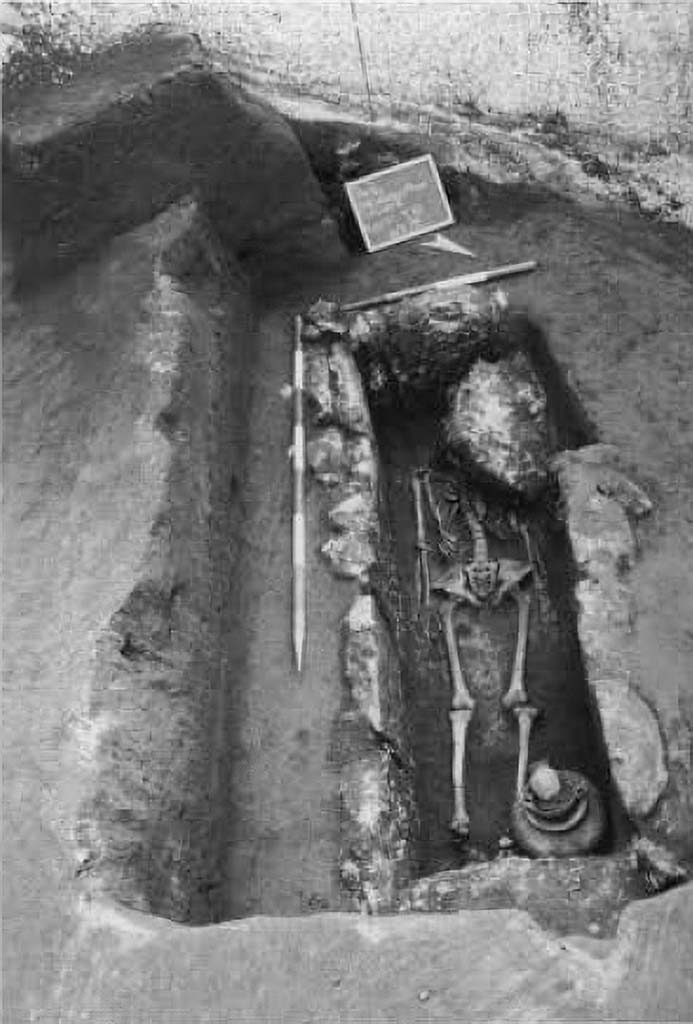Pompeii Porta Sarno Necropolis. 1999.
Skeleton in inhumation tomb from the Samnite period, encased in travertine blocks.
The first tomb explored contained a single skeleton with the head to the west. At the feet were the grave goods, consisting of an achromatic olla, a black varnished kylix, stamped with 6 rosettes joined by circular arcs, a black varnished oinochoe, with a round mouth. They are, as can be seen, poor burials dating back to between the mid-4th and the beginning of the 3rd century a. C. 
Scheletro in tomba ad inumazione di età sannitica, a cassa di blocchi di travertino.
La prima tomba esplorata conteneva un solo scheletro con testa ad ovest. Presso i piedi era il corredo, costituito da un'olla acroma, una kylix a vernice nera, con stampigliatura a 6 rosette congiunte da archi di cerchio, una oinochoe a vernice nera, con bocca rotonda. Sono, come si vede, sepolture povere databili tra la metà del IV e gli inizi del sec. III a. C. 
See/Vedi Suburbio Orientale in Rivista di Studi Pompeiani X, 1999, p. 180, fig. 1.