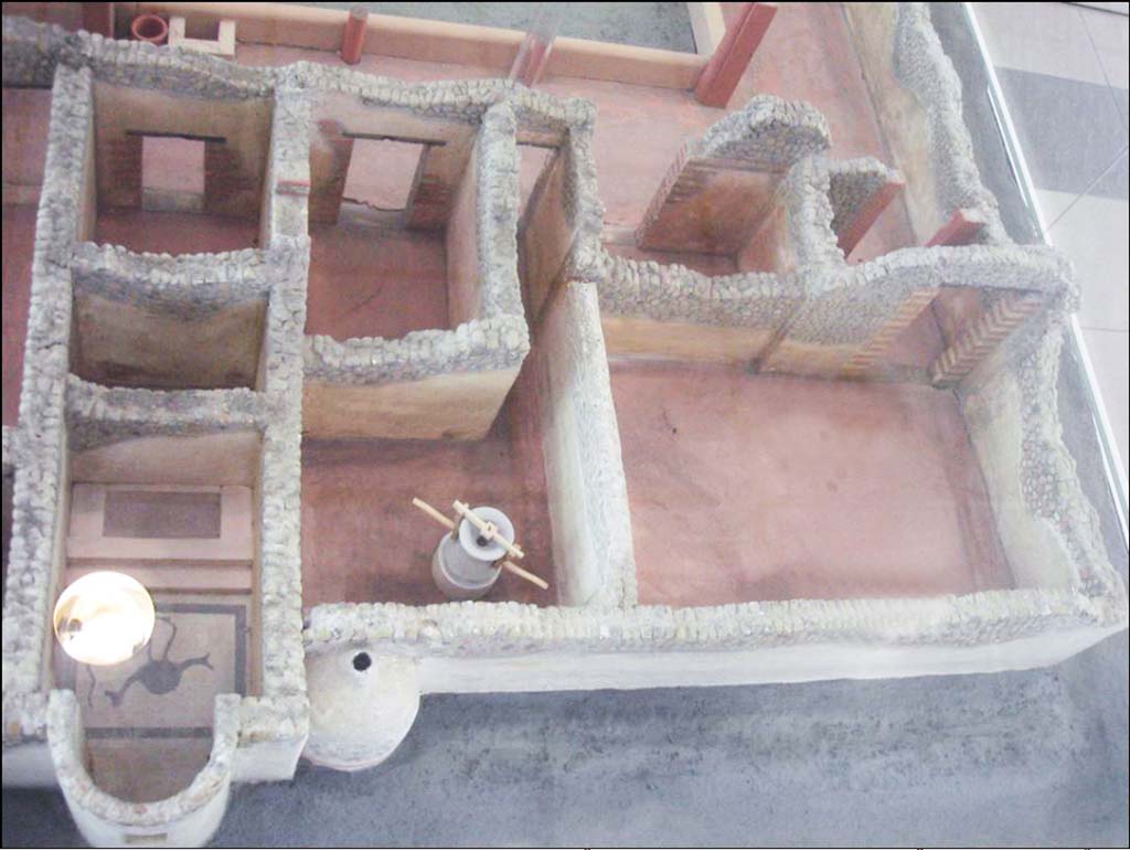 Villa della Pisanella, Boscoreale. The three rooms in the corner are cubiculum “D” (left rear), porters room “B” (right rear) and the large room “C” which was under the road at the time of excavation.
Centre is the room at the end of corridor “E” with grain mill and bread oven with triclinium “F” behind. 
Left are calidarium “O” with mosaic floor, boiler room “L” and cubiculum “G”. Model of villa in Boscoreale Antiquarium.