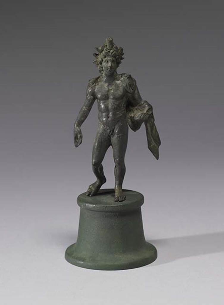 Boscoreale, Villa rustica in fondo D’Acunzo. Room 12, lararium. 
Bronze statuette of Alexander Helios, 0.13m high, front view.
A beautiful smiling Helios, he is portrayed nude, with a radiate crown upon his head. 
He wears a light veil falling from his shoulders and wrapping around his left forearm.
The left hand (with globe) was missing. 
A lorum (leather strap or thong) would have perhaps been the attribute carried downwards in the right hand.  
Photo courtesy of The Walters Art Museum, Baltimore. Inventory number 54.2290.
http://thewalters.org/
Creative Commons Attribution-ShareAlike 3.0 Unported Licence