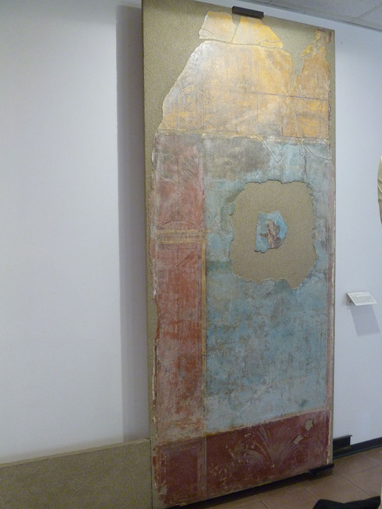 Boscoreale. Villa of Numerius Popidius Florus. Cubiculum 21. Part of fourth style north wall.
Cupid carrying a basket with low rim in the right hand, and a pedum (shepherd’s crook) in the left.
Erote portante con la d. un cesto a basso orlo, e con la sin. il pedum.
Photo courtesy of Michael Binns. Now in Boscoreale Antiquarium.
