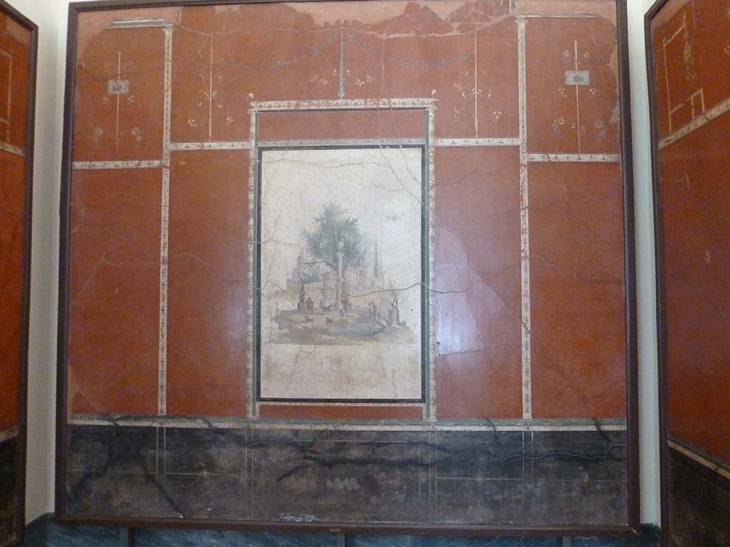 Villa Agrippa Postumus, Boscotrecase. May 2010. Room 16, north (rear) wall.
Now in Naples Archaeological Museum. Inventory number 147501.
A still-life depicting figs can be seen in the black ground dado/plinth of the rear wall. 
At the centre of the slender framed aedicule is a sacred landscape with shepherds and goats near a circular shrine and votive column, small panels with theatrical masks, delicate candelabra and branches with flowers complete the decorative ensemble in the upper zone.