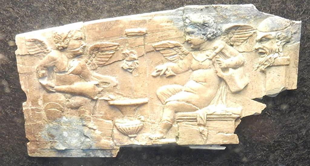 Villa Rustica di Marcus Livius Marcellus. Ivory plaque found in a cubiculum. On the right is a pilaster on which is a bearded head in relief (Silenus?).
Left and centre are two cupids, one holding a lyre and the other pouring wine from an amphora into a krater which is near a fountain with a mask on a pilaster.
Photo courtesy of Buzz Ferebee.
See Notizie degli Scavi di Antichità, 1929, p. 185, fig. 7.