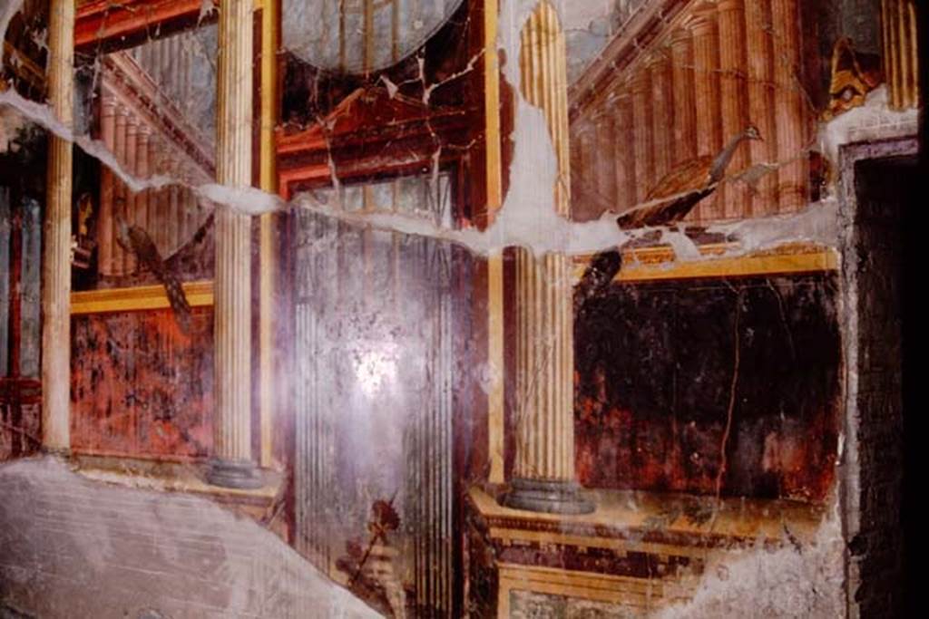 Oplontis Villa of Poppea, 1974. Room 15, detail of painted lower east wall in oecus. 
Photo by Stanley A. Jashemski.   
Source: The Wilhelmina and Stanley A. Jashemski archive in the University of Maryland Library, Special Collections (See collection page) and made available under the Creative Commons Attribution-Non Commercial License v.4. See Licence and use details. J74f0669
In the centre is an Apollonian torch, at the side is a bucranium and above is a Delphic tripod resting on a podium, all attributes of Apollo designed to show the divinity of Apollo and show the way through the gates on either side in an artistic portrayal of a sanctuary of Apollo.