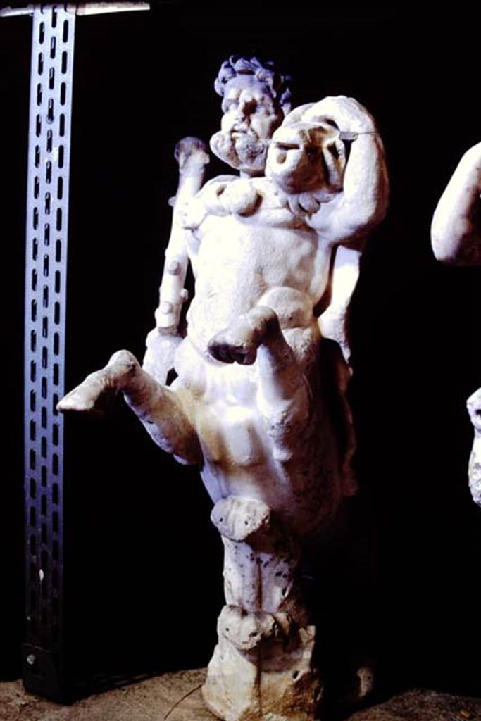 Oplontis Villa of Poppea, 1977. One of a group of four centaurs, a male holding a club with a small boar on his shoulder. 
Two centaur fountains had been on each side of the passageway.
There was no evidence of pipes, so they had not been used as fountains in their final location.
Photo by Stanley A. Jashemski.   
SAP inventory number 70068.
Source: The Wilhelmina and Stanley A. Jashemski archive in the University of Maryland Library, Special Collections (See collection page) and made available under the Creative Commons Attribution-Non Commercial License v.4. See Licence and use details.
J77f0340
According to De Caro, a group of four centaurs were found under portico 33 on 17th February 1970. 
When they were found, they were very badly damaged. Heads and limbs were mostly detached and it was necessary to provide patient and pain-staking work of re-composition. 
See De Caro, S.1976. Sculture dalla villa “di Poppea” in Oplontis (p.198) in Cronache Pompeiane, II, 1976, (p.184-225)