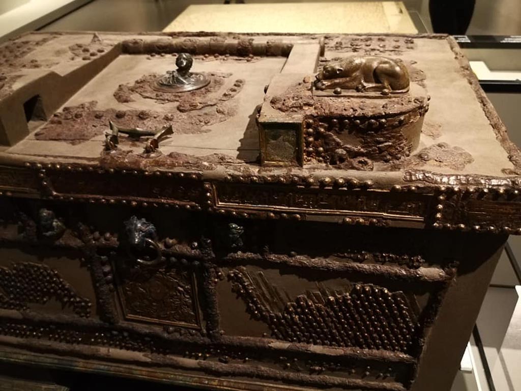 Oplontis, Villa of Lucius Crassius Tertius. December 2019. Strongbox, detail of lid with female protome, bronze dog from right side, and the lion’s head and cupids on the front.
On display in exhibition “Pompei e Santorini” in Rome, 2019. Photo courtesy of Giuseppe Ciaramella.
The owner first had to move the female head in the centre of the lid that concealed the lock. The inner iron bars were pushed outwards by pulling the lion's head, and the safe was definitively opened only after turning the head of a cupid.