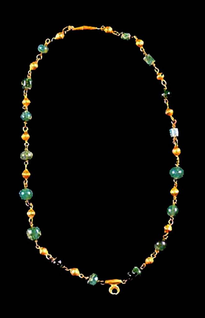 Oplontis, Villa of Lucius Crassius Tertius. Necklace found in room 10, in 1984, under the head of skeleton no. 14.
It comprised of 16 green stones alternated with 18 small spheres with gold foil. 
It has a pendant of a small crescent moon.
See D’Ambrosio A., 1987. Rivista di Studi Pompeiana I, p. 176, fig. 45.
Oplontis inventory number 3307.
See D’Ambrosio, A., 2001. Women and Beauty in Pompeii. Roma: Bretschneider, p. 56, fig. 20.