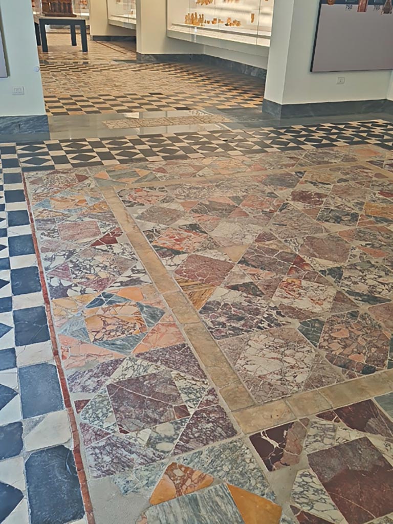 Mosaic in Naples Archaeological Museum, from room 13 of Secondo Complesso. June 2024. 
Looking from first room (CXLIII) towards second room (CXLII). Photo courtesy of Giuseppe Ciaramella.
According to Miele -
From oecus 13 of the so-called Second Stabiae Complex…….comes the panel, now in room CXLIII, with rows of marble squares in Portasanta and Pavonazzetto surrounded by a band of cipollino………………………. The central panel of the same oecus 13 is found, however, in room CXLII.
See Miele, F., 2019 in MANN. La Collezione Magna Grecia. Electa, Milano, page 66-7.