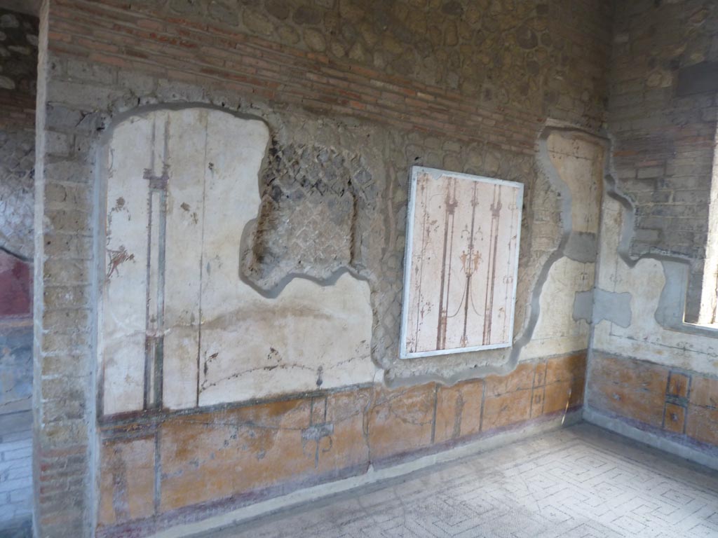 Stabiae, Villa Arianna, September 2015. Room 12, east wall.
The room was decorated with a yellow zoccolo (dado) and walls with white background.
According to the description board, the wall decoration was very refined but was much damaged during the Bourbon times.
The decoration showed slender chandeliers with human figures leaning on its arms, along with birds, grasshoppers and butterflies.