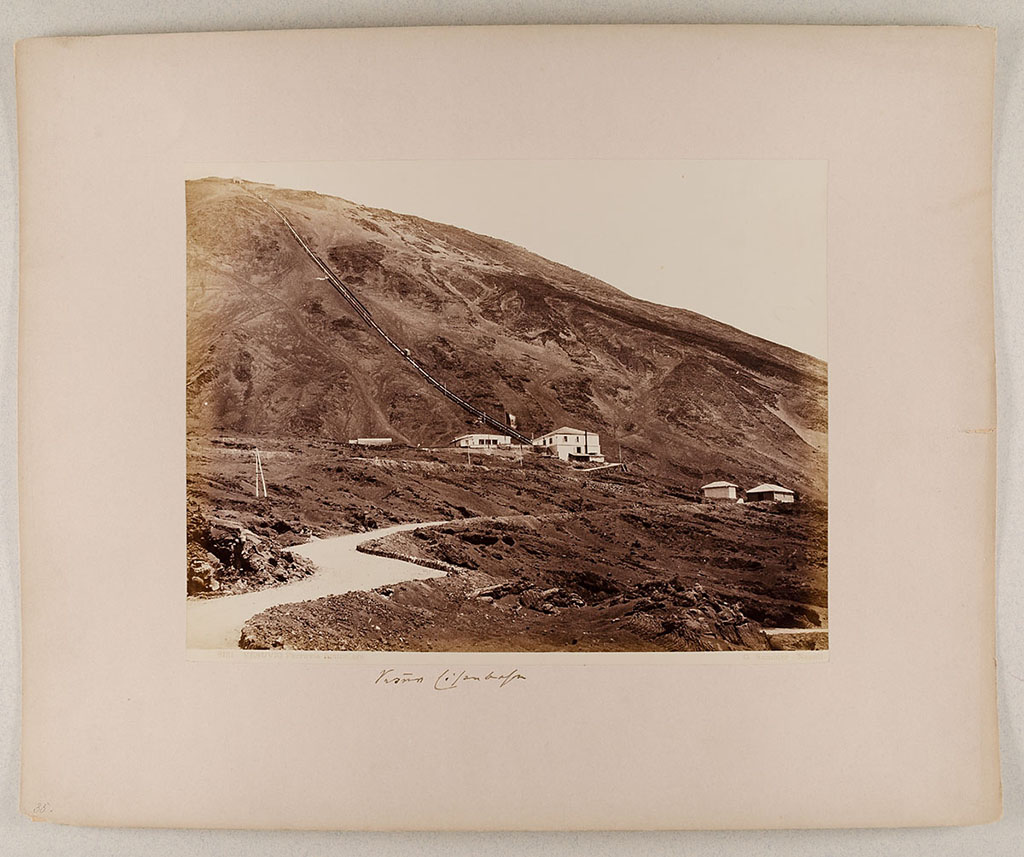 Vesuvius Funicular railway. 1880-1890 photo of the lower station and the track up to the summit.
Photo title at bottom is "8121 Vesuvio. Ferrovia funicolare. G. Sommer – Napoli”. 
The handwritten note says "Vesuv Eisenbahn".
Museum für Kunst und Gewerbe Hamburg, inventory number P1981.400 (Public Domain).
See https://sammlungonline.mkg-hamburg.de/de/object/8121-Vesuvio.-Ferrovia-funicolare/P1981.400/mkg-e00135742