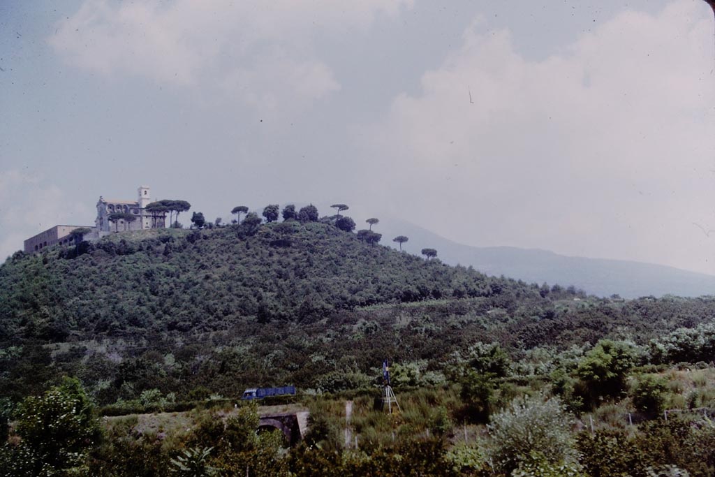 Missionari Redentoristi Colle Sant'Alfonso. 1964. Photo by Stanley A. Jashemski.
It sits on a hill of volcanic origin, S. Maria La Bruna, 185 metres high with Vesuvius behind to the north.
According to the church web site “the hill has suffered little from the devastating effects of nearby Vesuvius, from which a large valley separates it, enough to protect it from lava eruptions”. 
The hill and church are a very prominent landmark to anyone travelling along the A3 autostrada who looks north towards Vesuvius.
Source: The Wilhelmina and Stanley A. Jashemski archive in the University of Maryland Library, Special Collections (See collection page) and made available under the Creative Commons Attribution-Non-commercial License v.4. See Licence and use details.
J64f1138